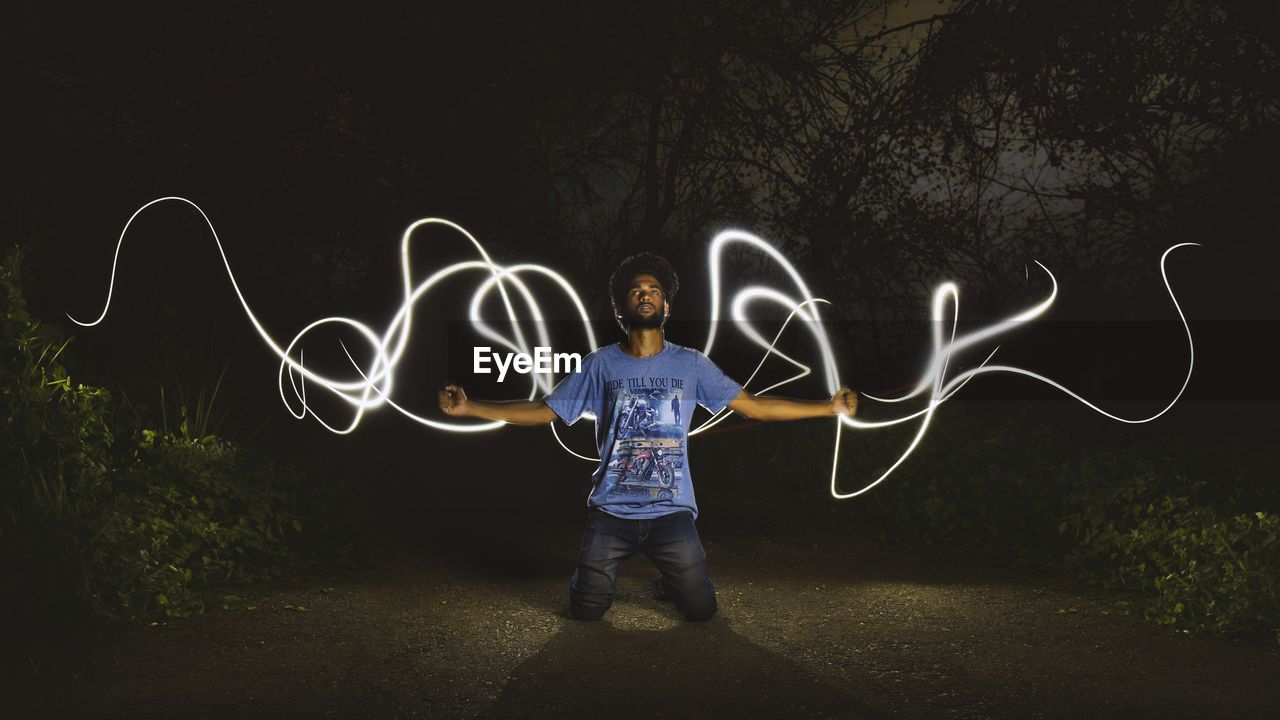 FULL LENGTH OF YOUNG MAN STANDING AGAINST ILLUMINATED LIGHT