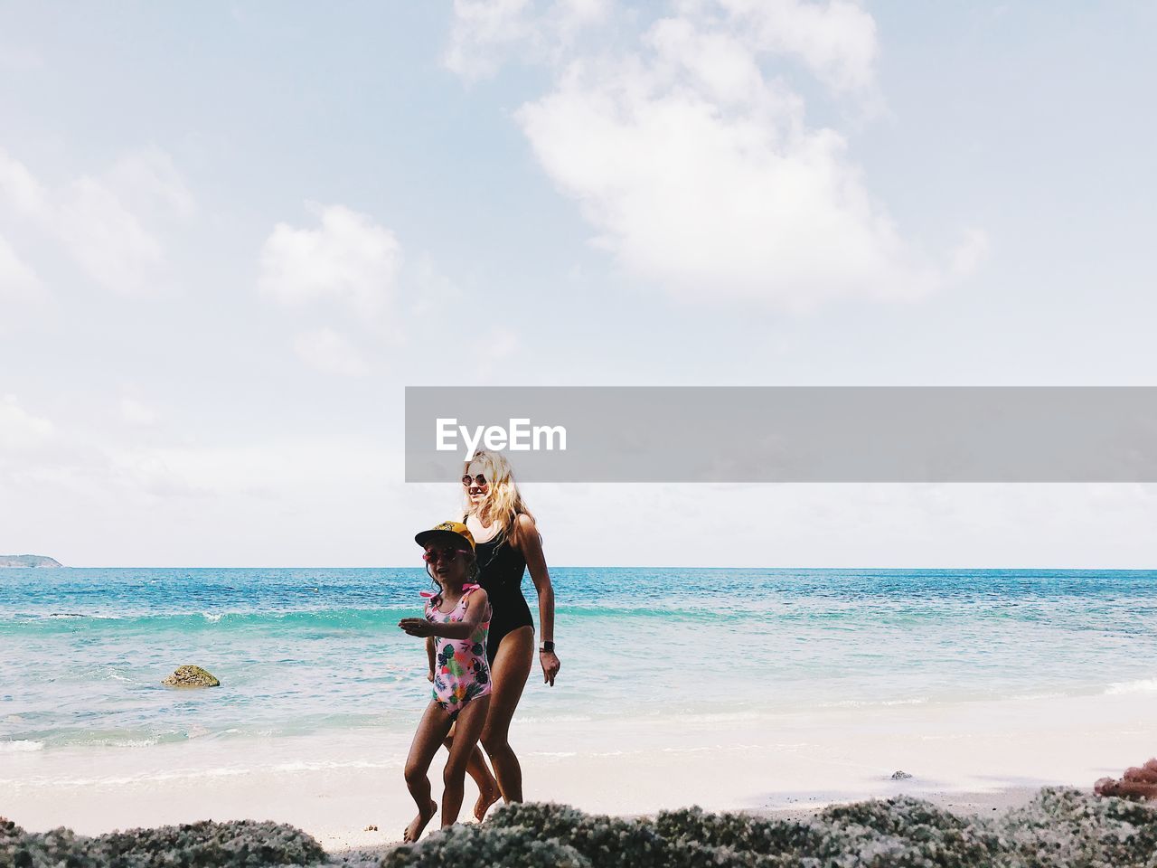 Mother and daughter at beach against sky