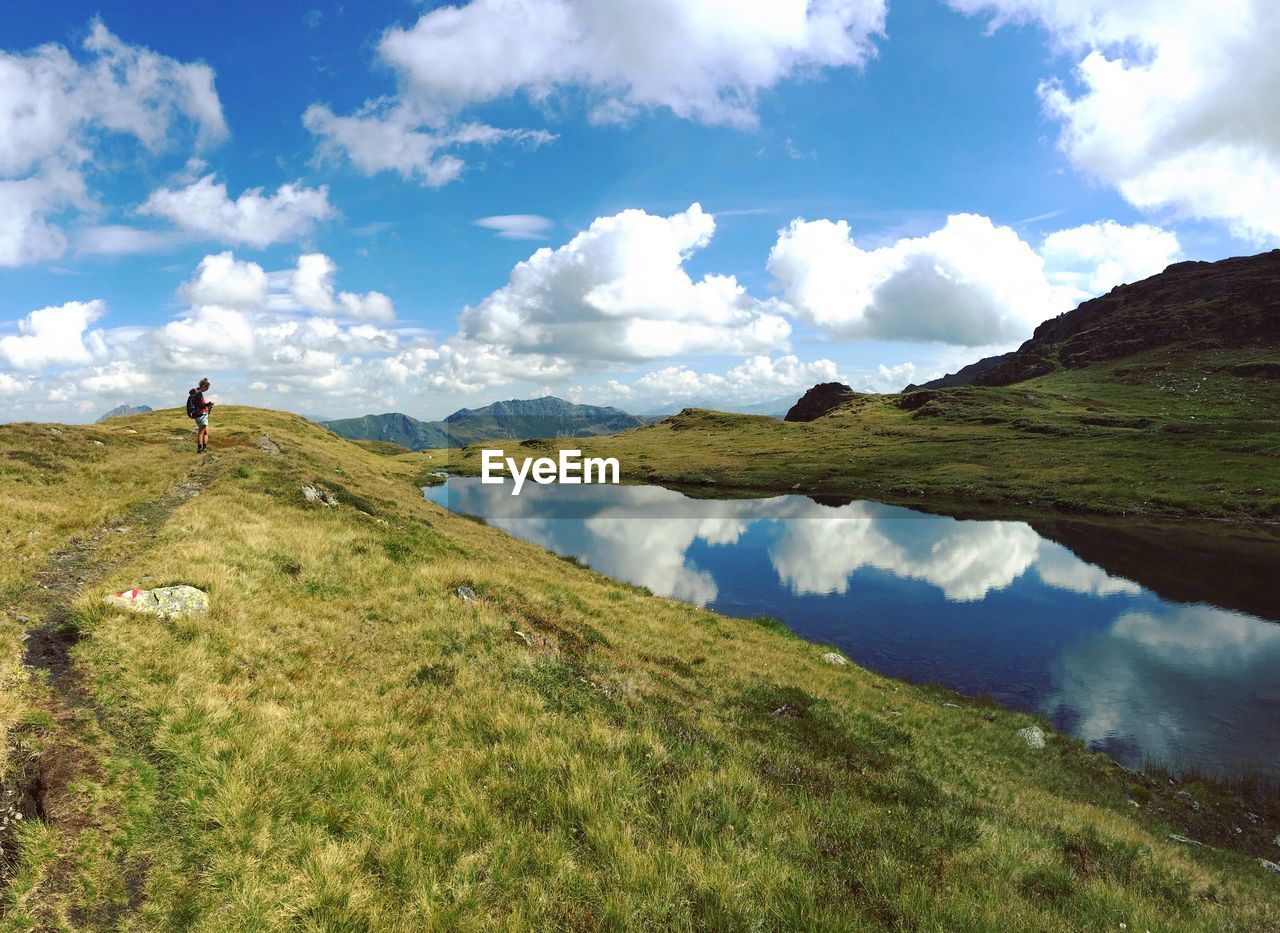 Distant view of woman on field by lake against cloudy sky