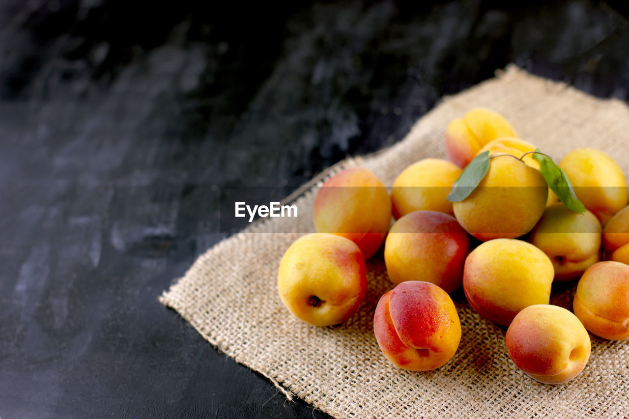 Fresh apricot on a sackcloth on black wooden table. ripe sweet berries in droplets of water