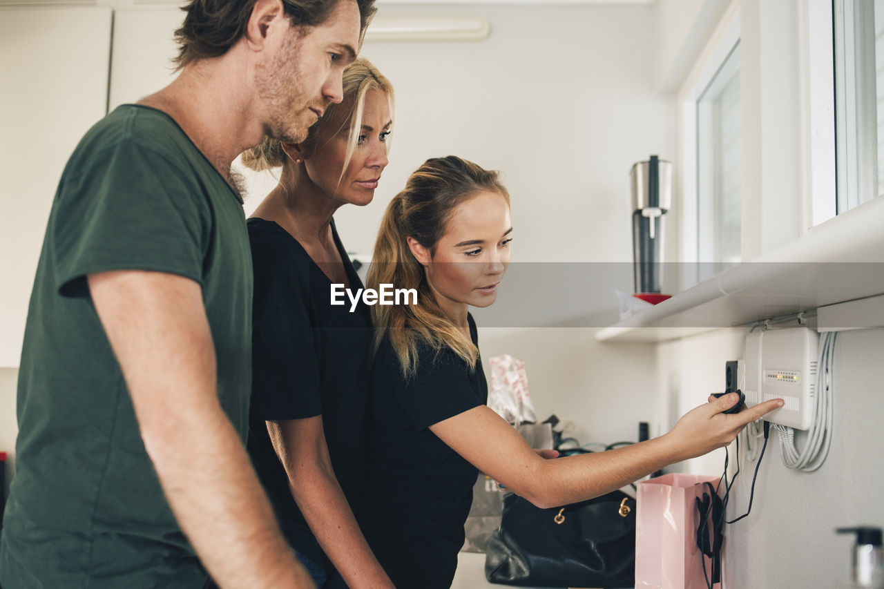 Teenage girl pointing at equipment mounted on wall to parents at home