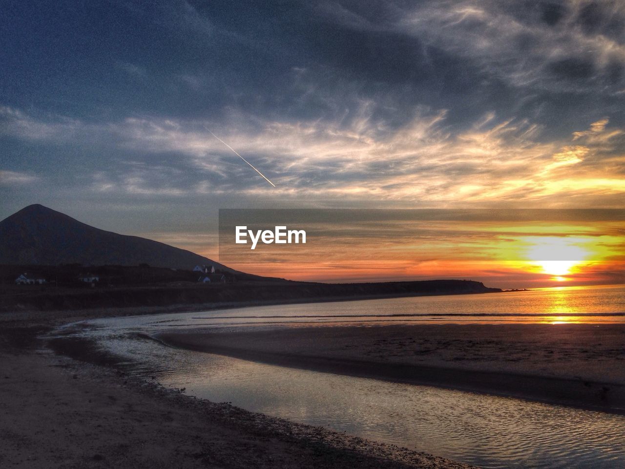 Idyllic view of sunset over beach against cloudy sky