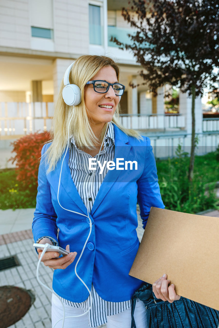 Businesswoman listening music on headphones against office building