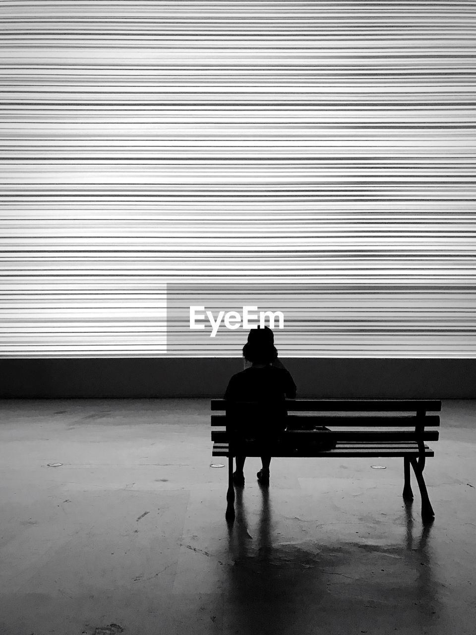 Rear view of person sitting on bench against wall