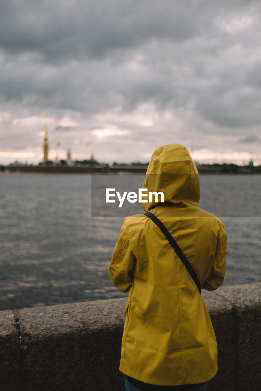 Woman traveler in yellow raincoat looking forward on dramatic landscape. 