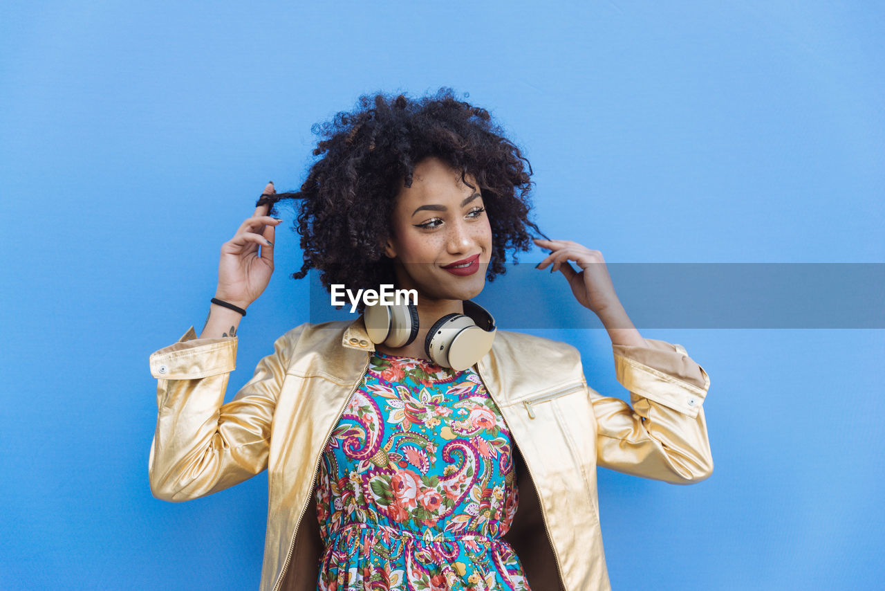 Fashionable young woman with curly hair against blue background