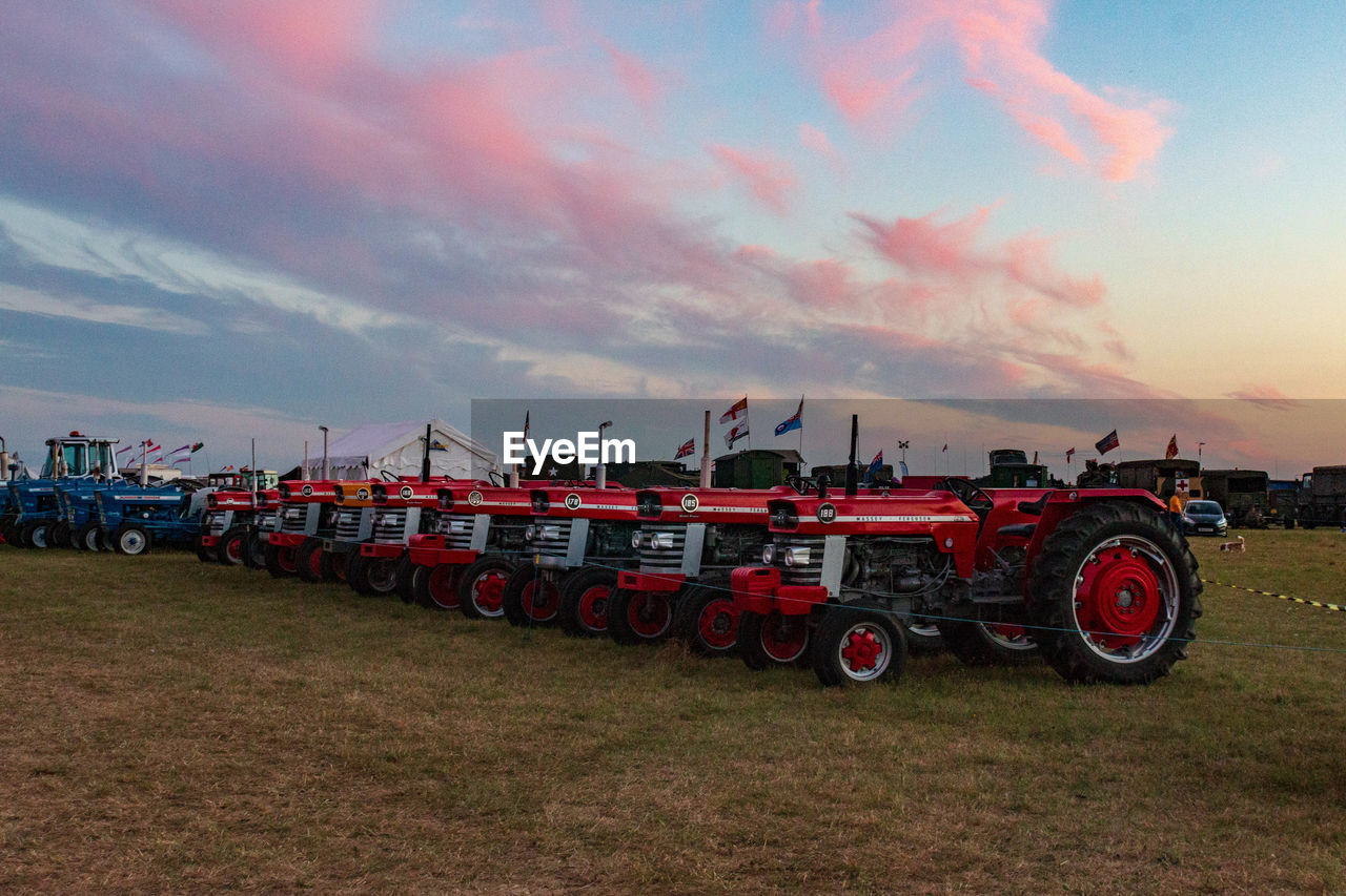 PANORAMIC VIEW OF RED CARS ON FIELD AGAINST SKY DURING SUNSET