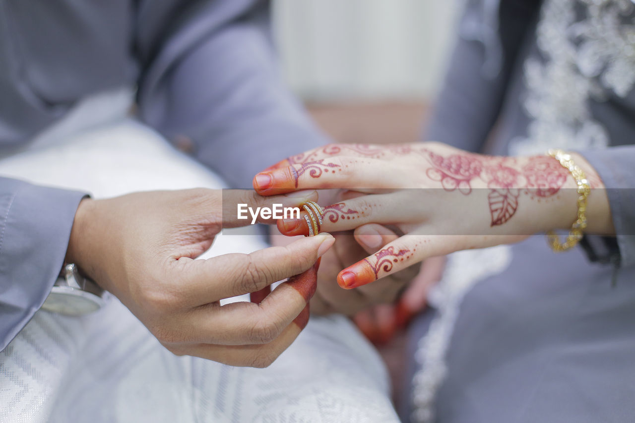 Midsection of groom exchanging ring with bride during wedding