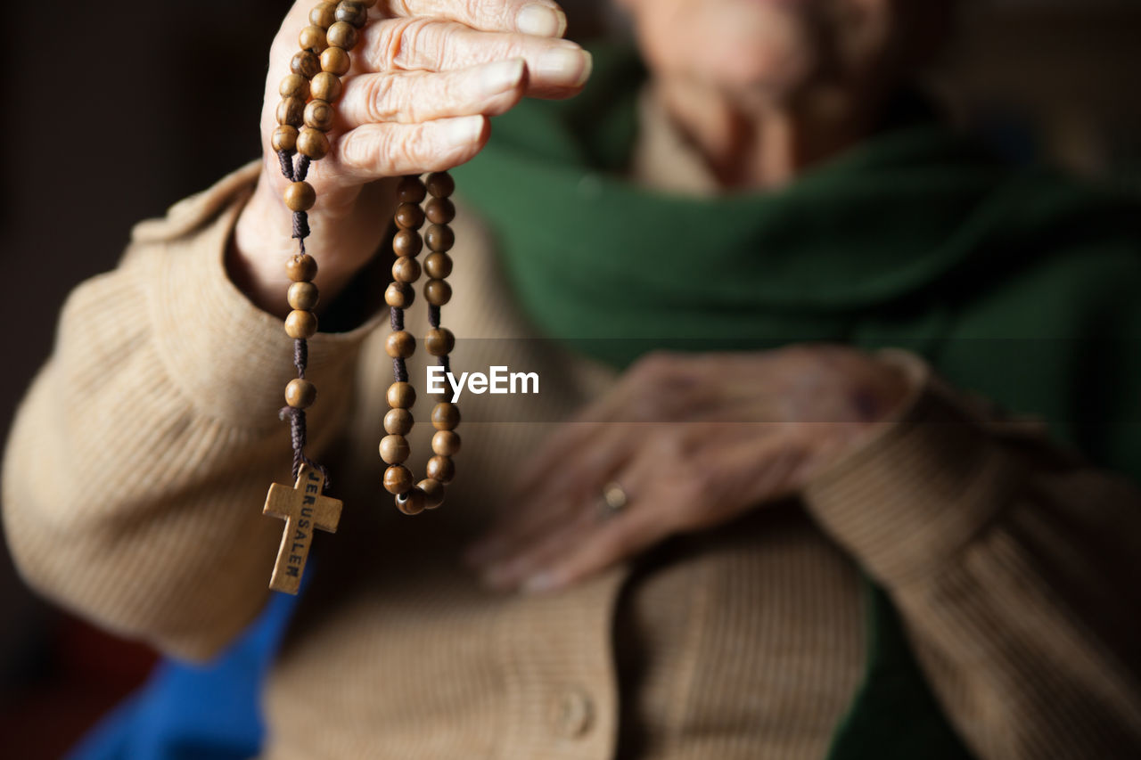 Midsection of senior woman holding wooden rosary beads with cross