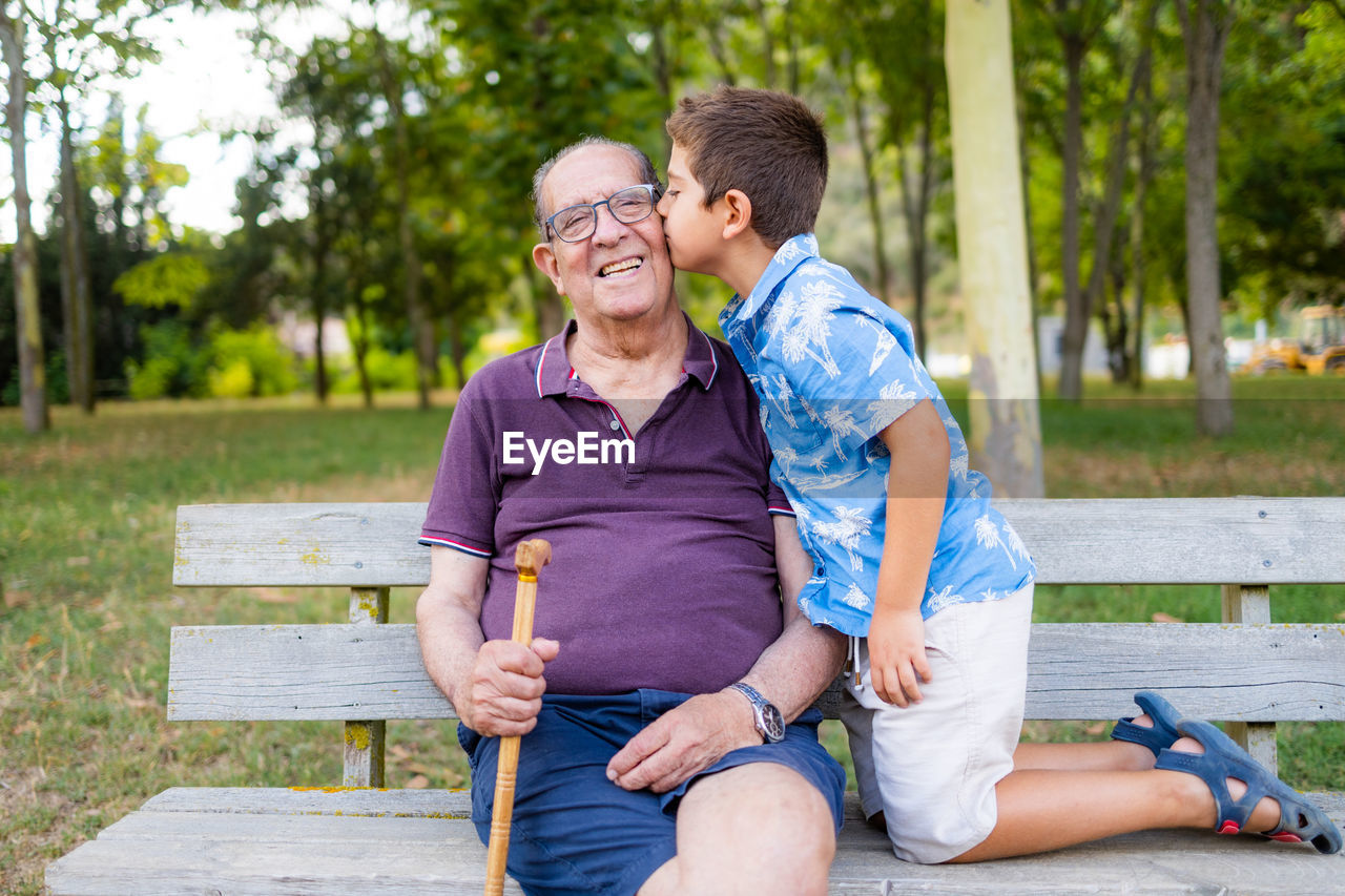 Gradson kissing his grandfather sitting on a bench in the park