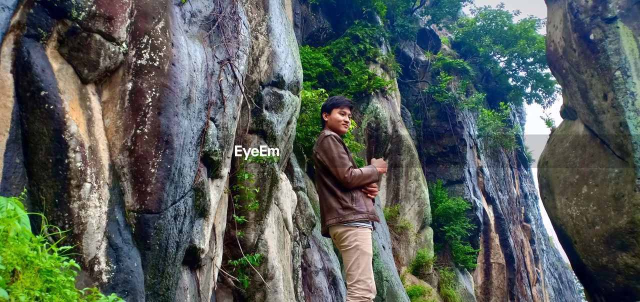 Man standing against rocks and plants in forest