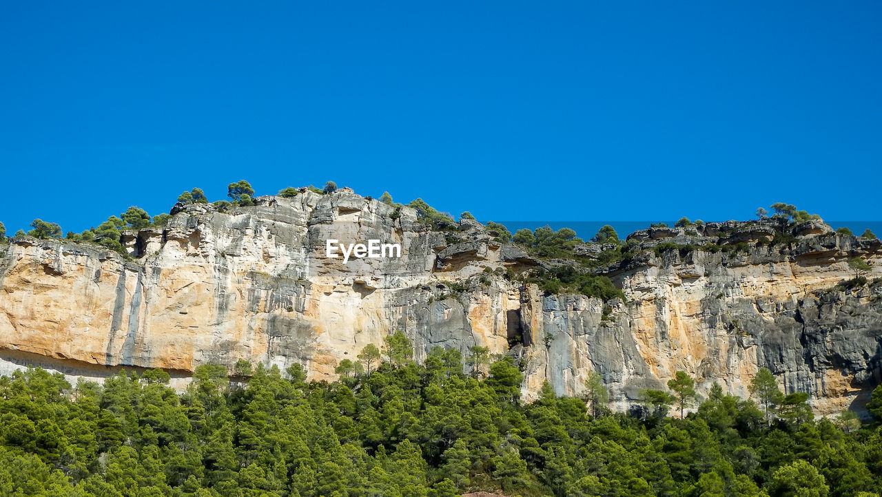 Low angle view of rocks against clear blue sky