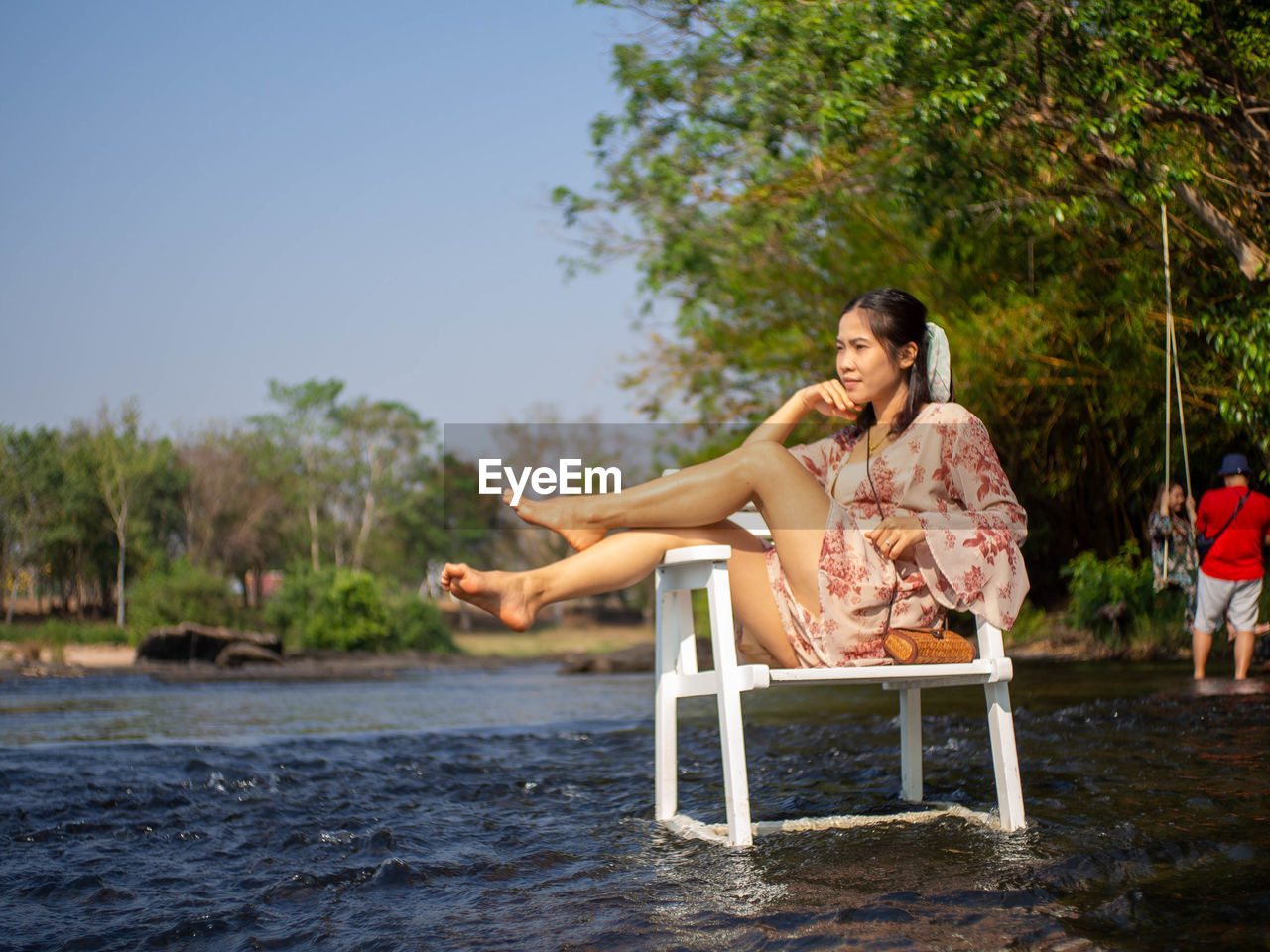 Woman sitting on a tree by plants against sky