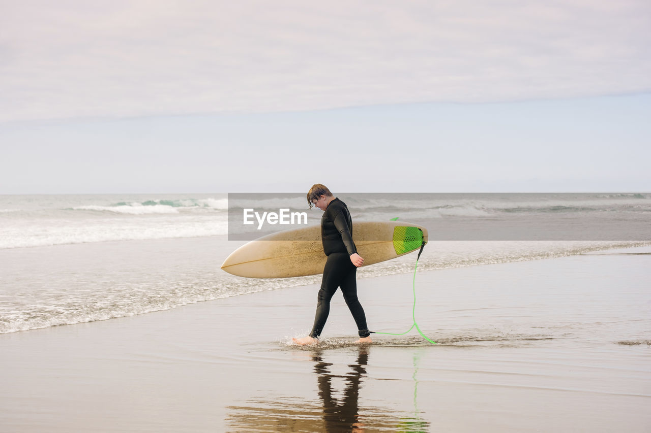 Boy walking into the water holding a surfboard at the beach