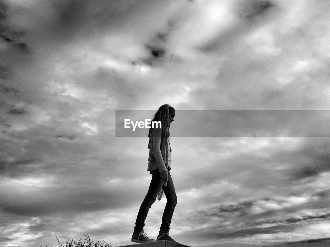 Side view of teenage girl walking against cloudy sky