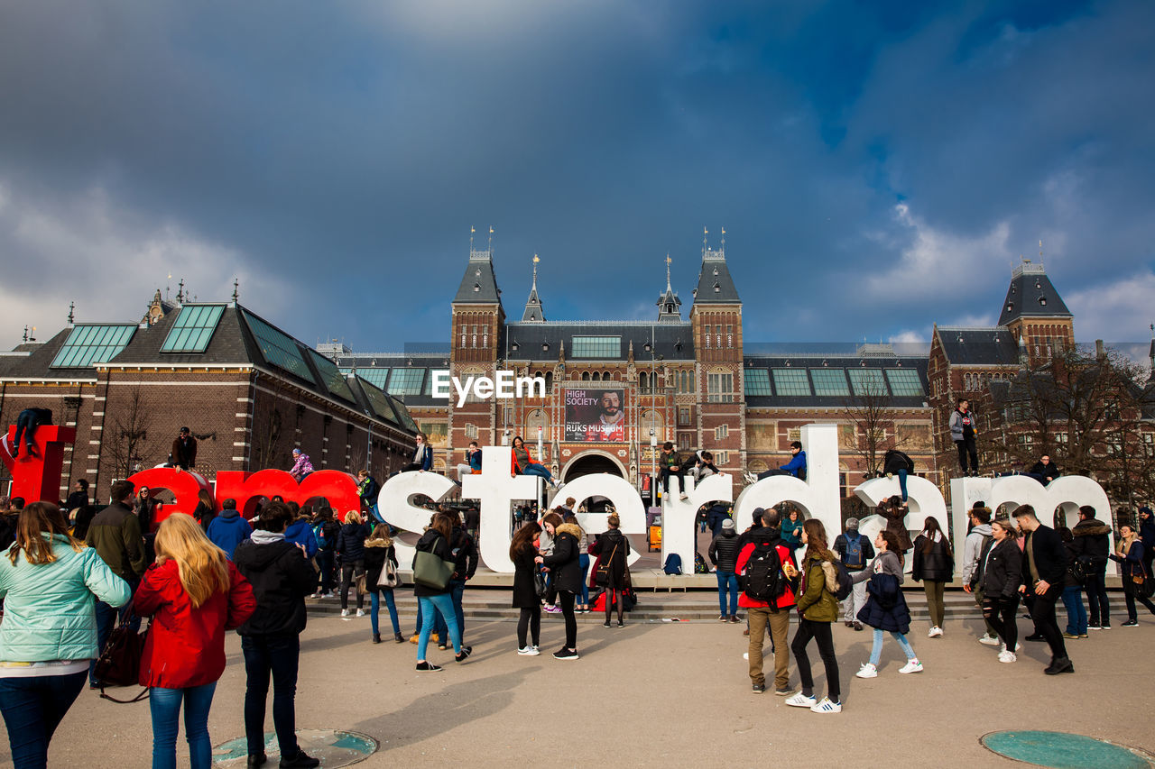 PEOPLE AT TOWN SQUARE AGAINST CLOUDY SKY