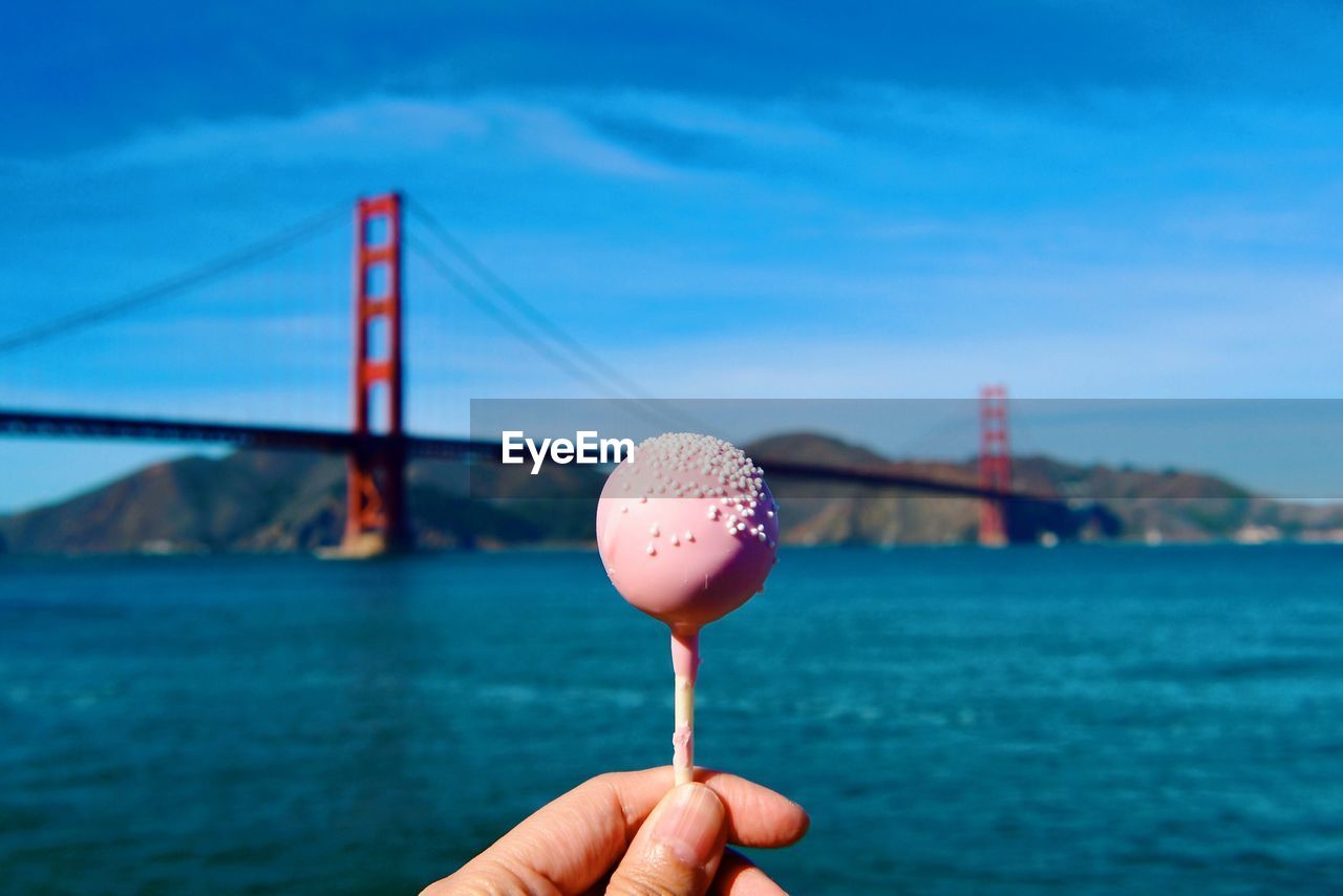 Cropped image of person holding lollipop against golden gate bridge