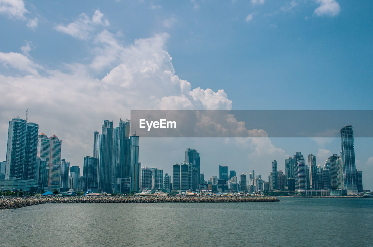 City at waterfront against cloudy sky