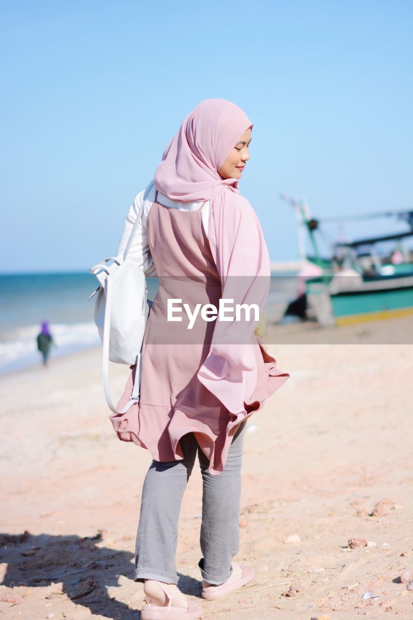 Woman wearing hijab walking at beach on sunny day