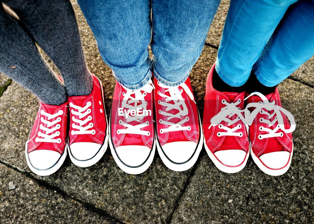 Low section of friends wearing red and white canvas shoes standing in row on footpath