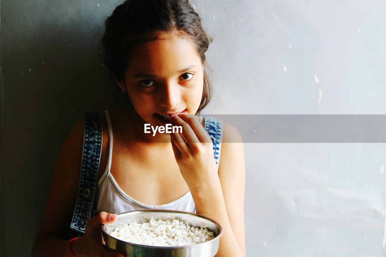 Portrait of girl eating popcorn against wall