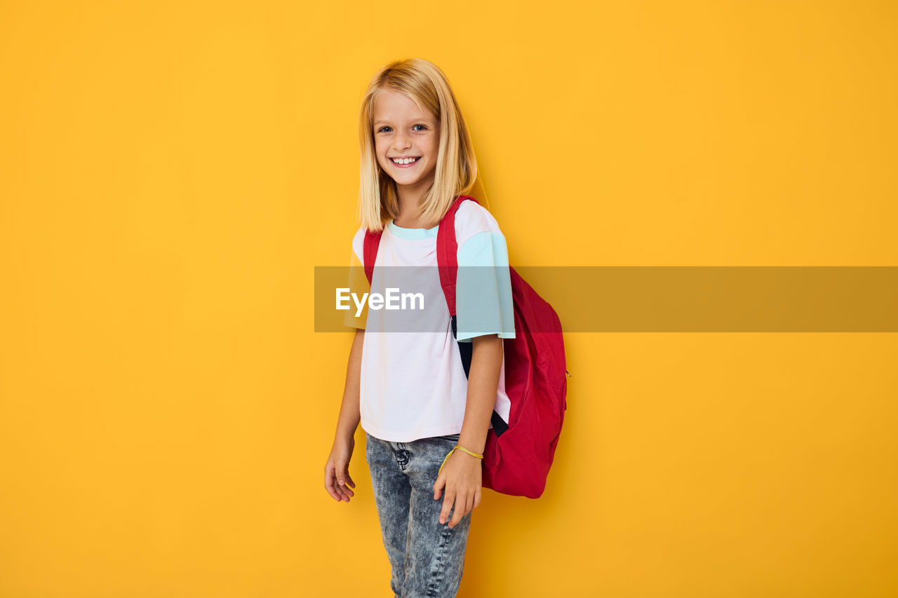 portrait of smiling young woman standing against yellow background