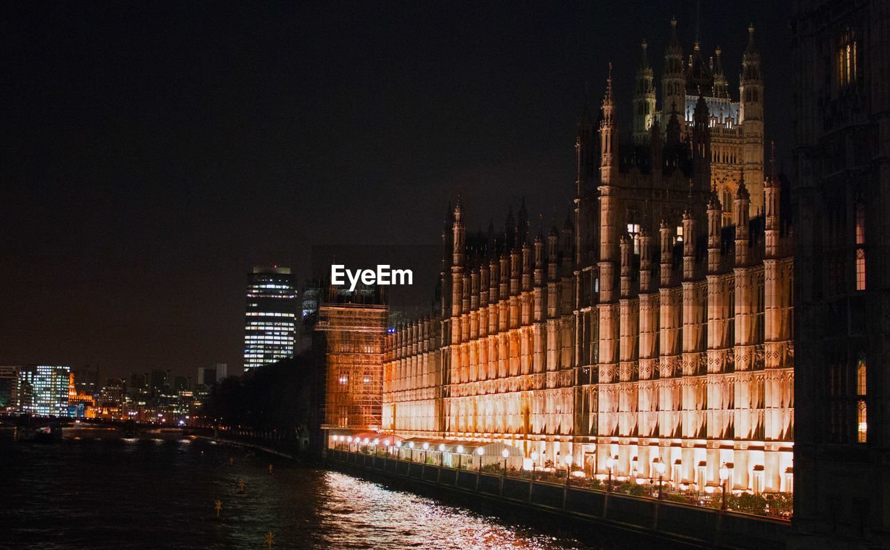 Illuminated houses of parliament by thames river against sky