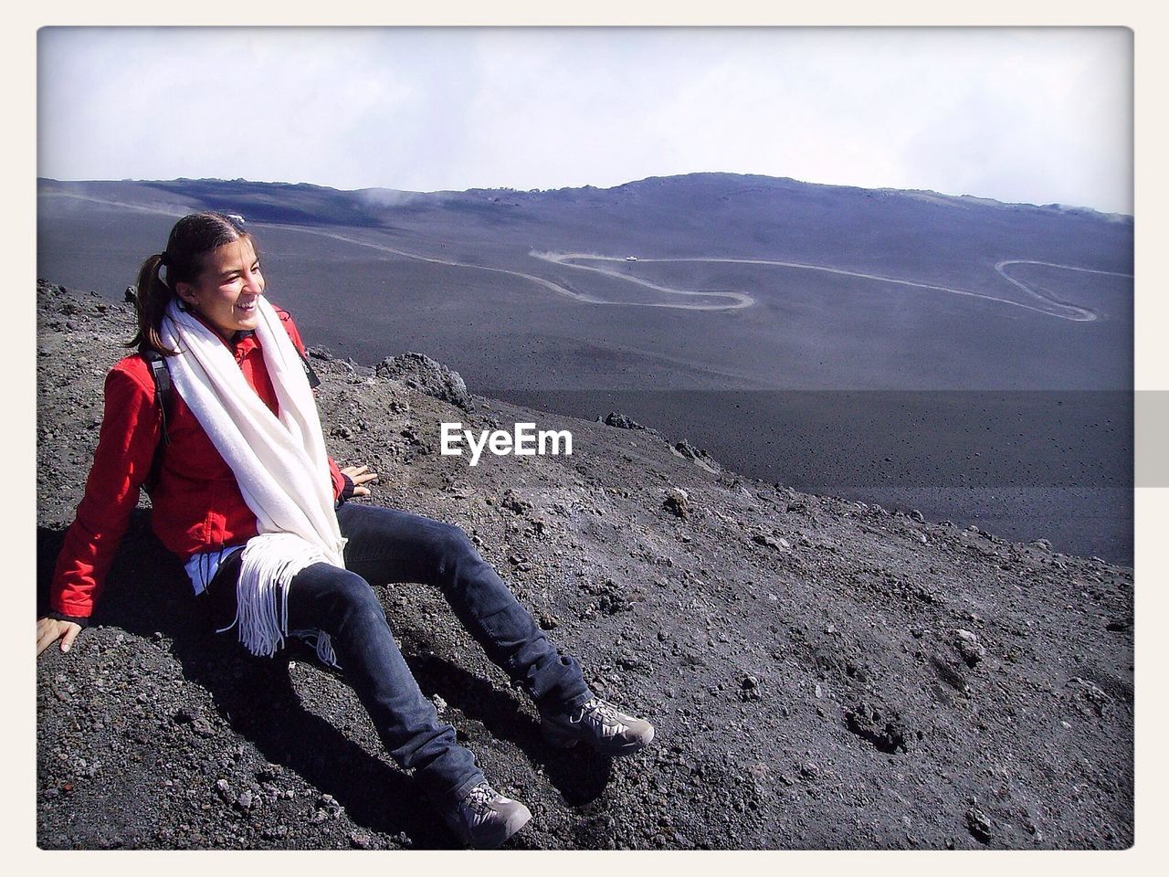 Full length of woman sitting of field at mt etna against sky