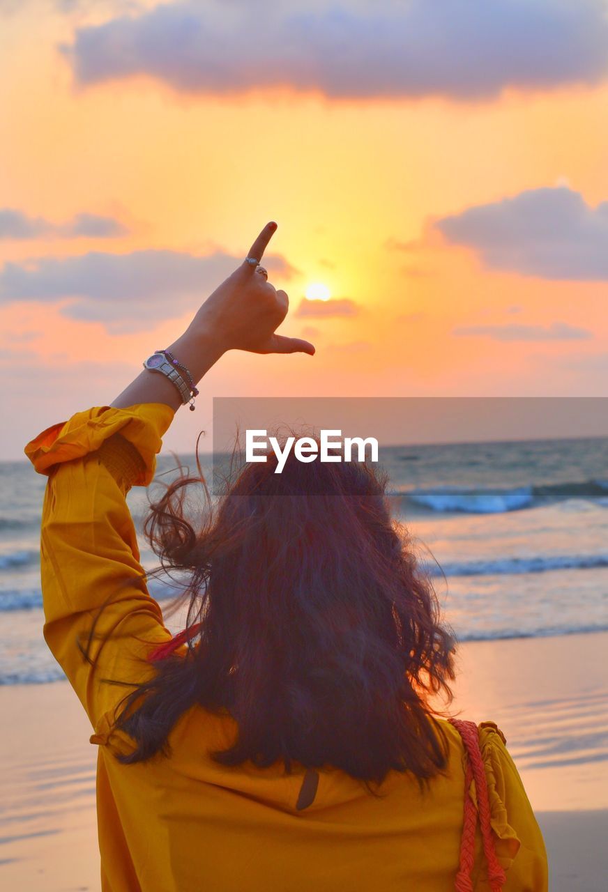 Rear view of woman gesturing shaka sign at beach during sunset