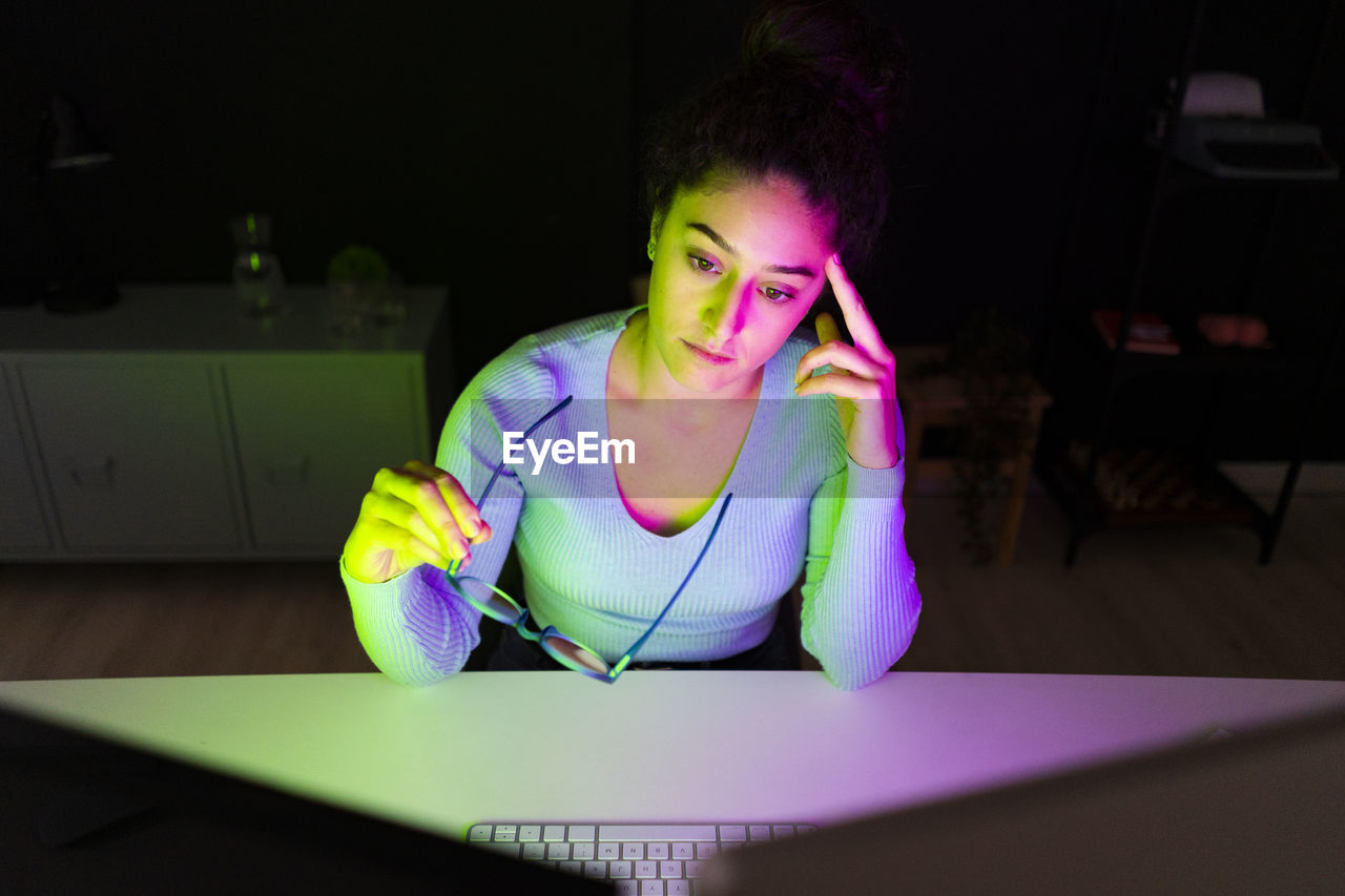 Worried businesswoman holding eyeglasses looking at desktops at home office