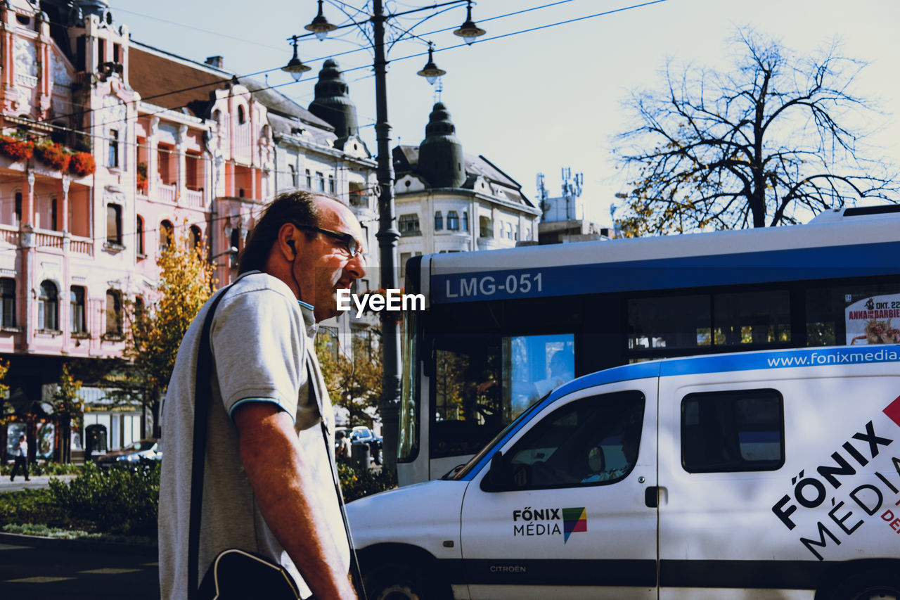 SIDE VIEW OF MAN STANDING ON CAR AGAINST SKY