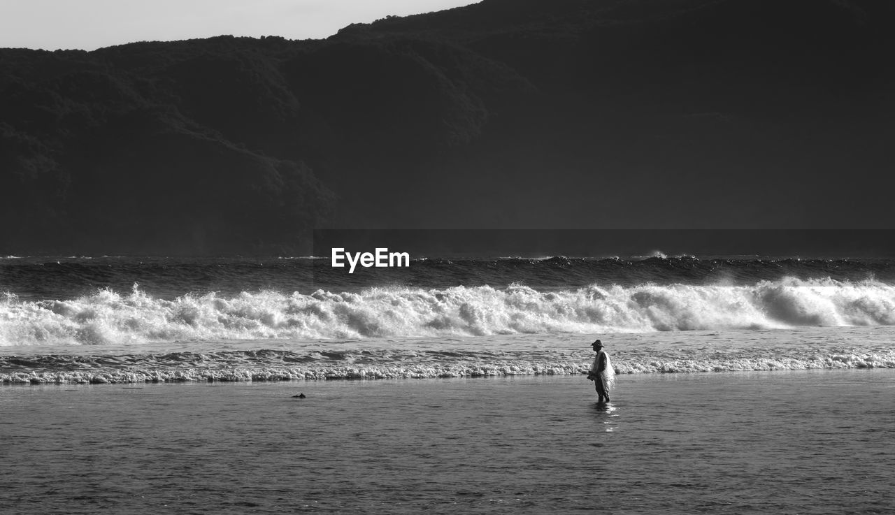 Person standing in sea against mountain