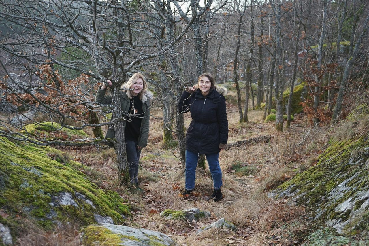 Full length portrait of happy friends standing against trees on field at forest