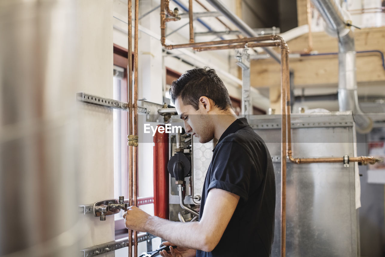 Side view of auto mechanic student analyzing machinery in workshop