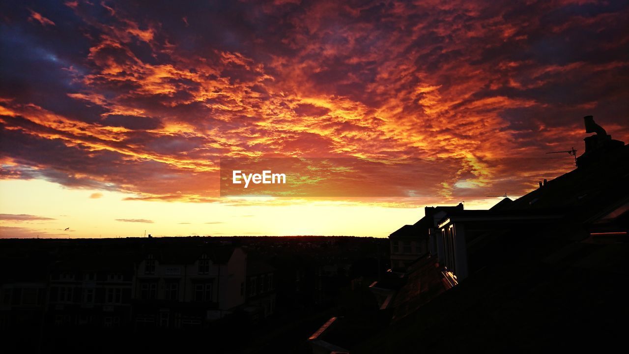 SILHOUETTE BUILDINGS IN TOWN AGAINST DRAMATIC SKY