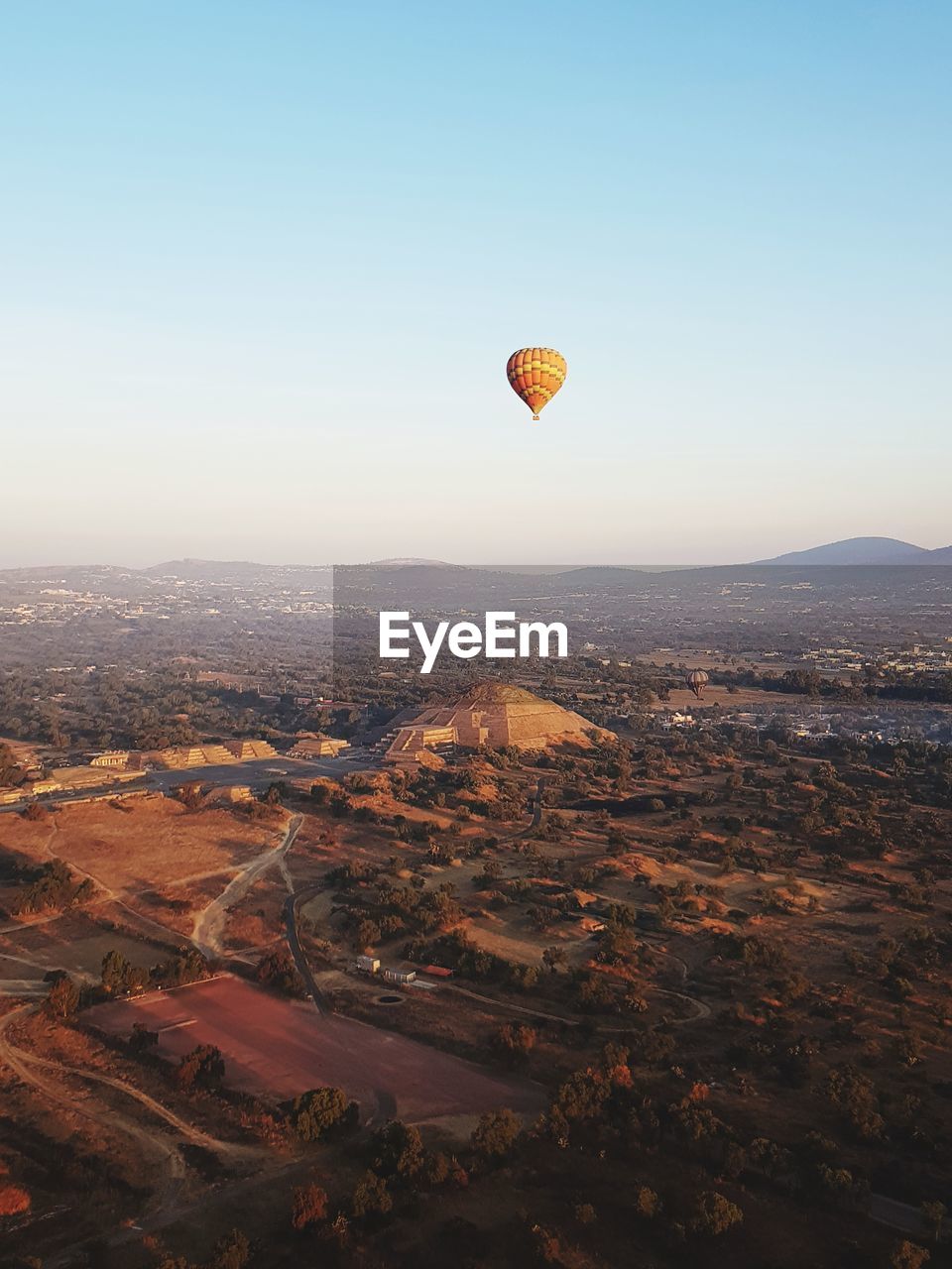 Hot air balloon flying over landscape and ancient pyramid against sky