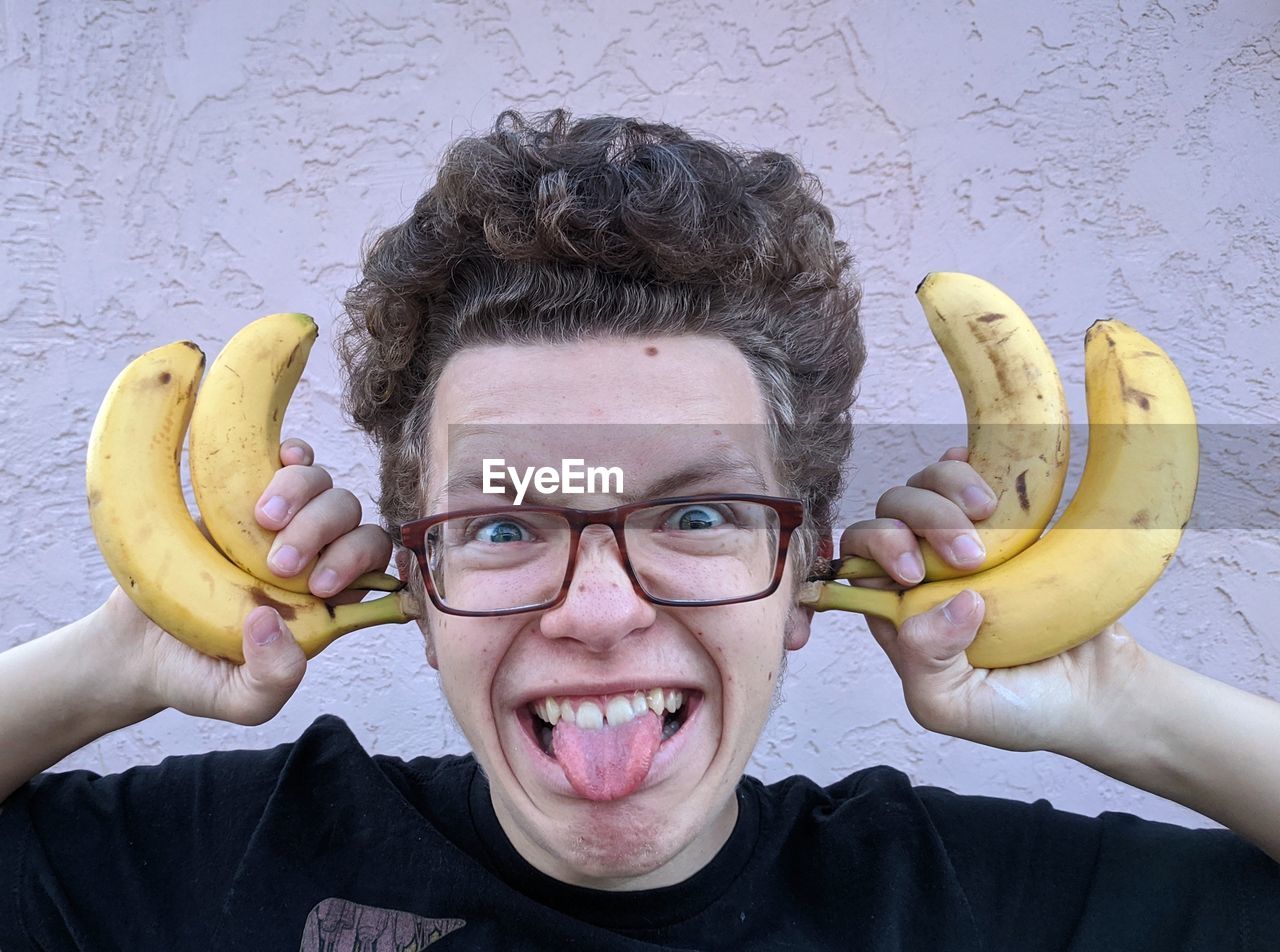 Portrait of teenage boy making a funny face and holding bananas by his head
