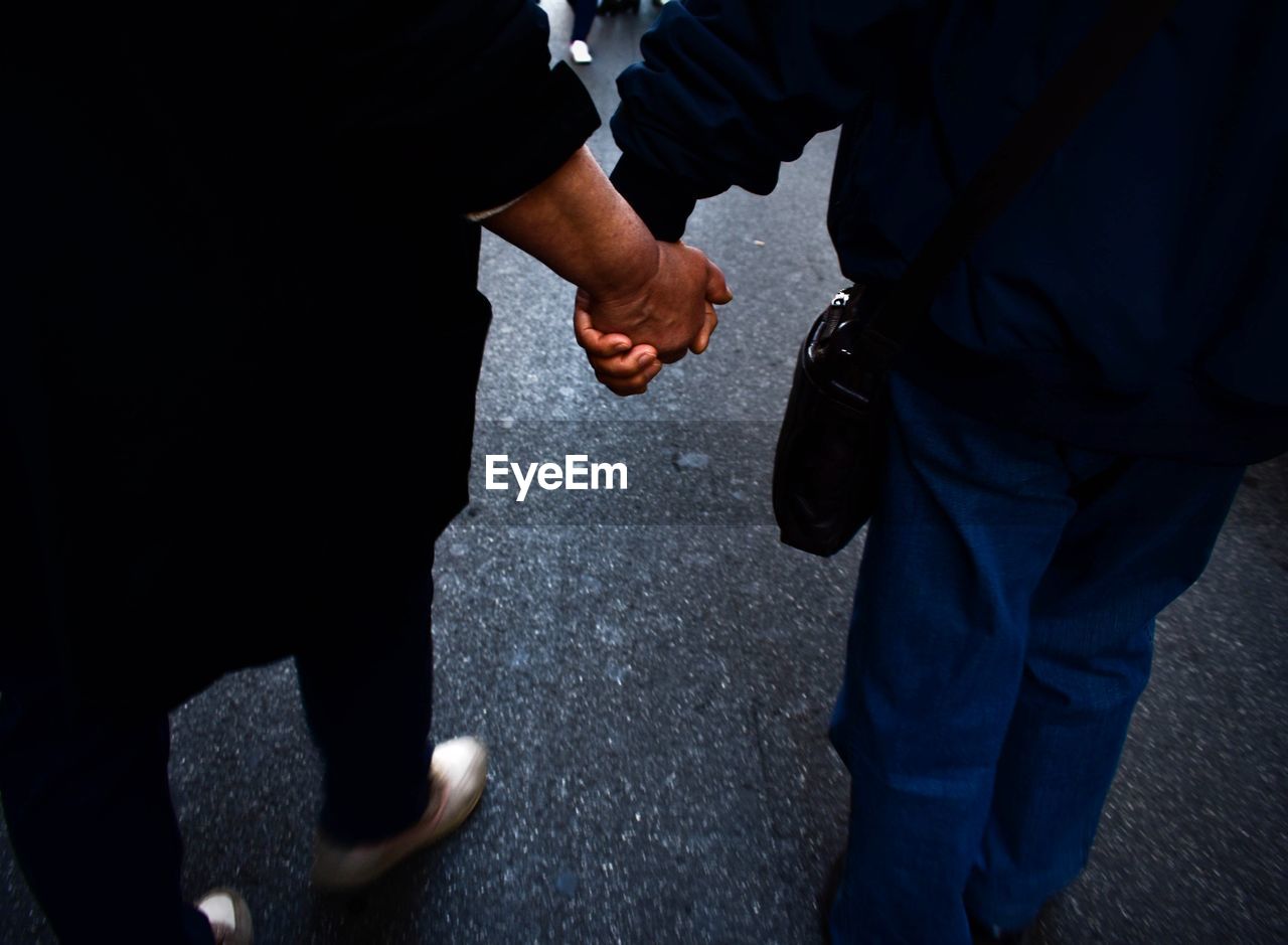 Low section of friends holding hands while walking on street