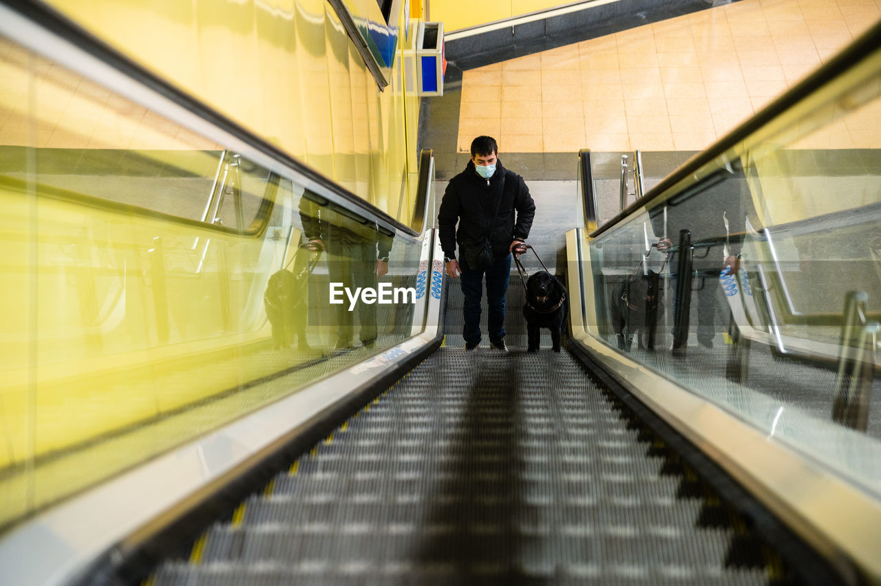 Blind man walking on escalator with guide dog