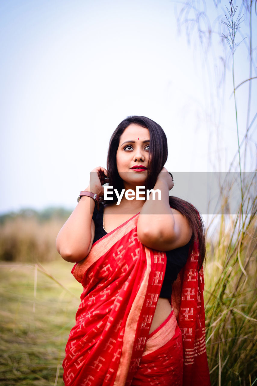 Portrait of beautiful young woman on field against sky