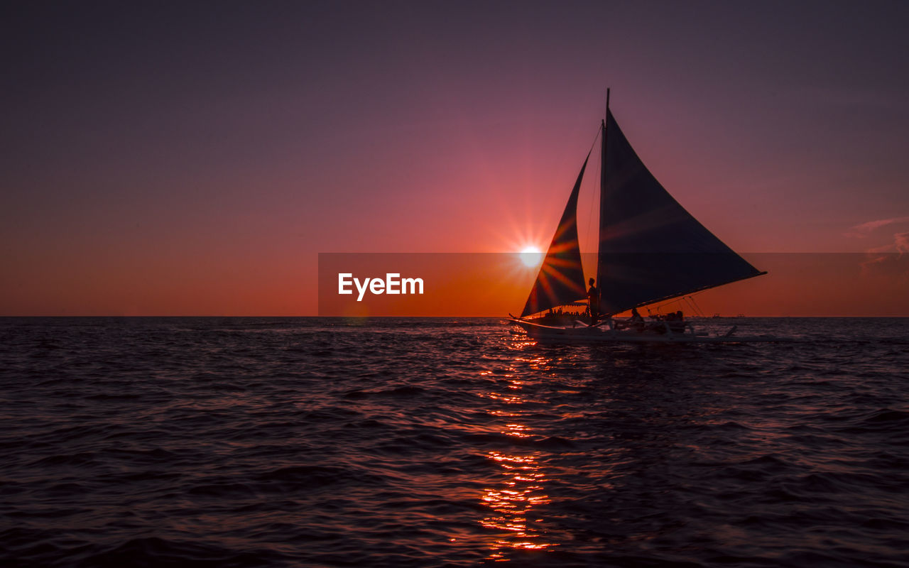 Silhouette sailboat sailing on sea against clear sky during sunset