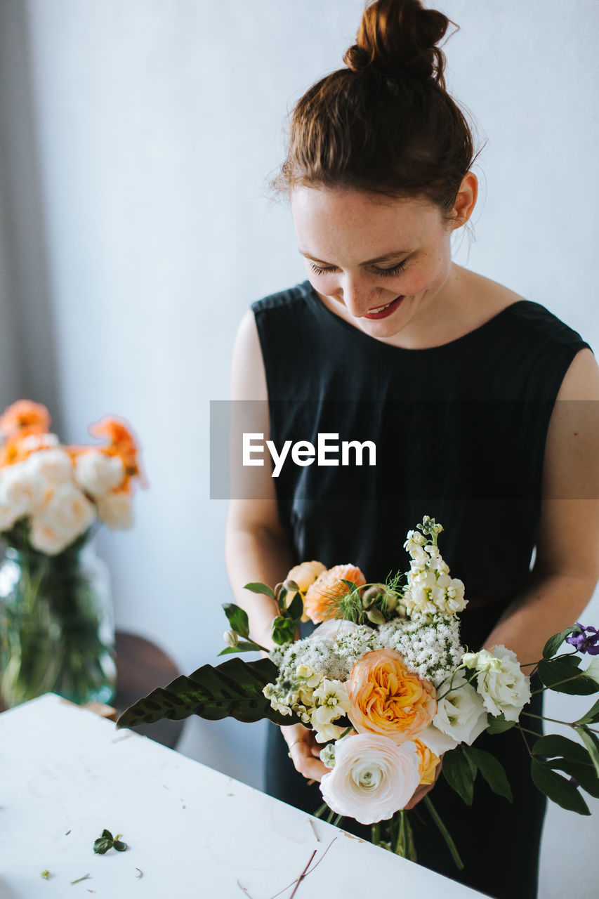 High angle view of woman arranging flowers in vase at table