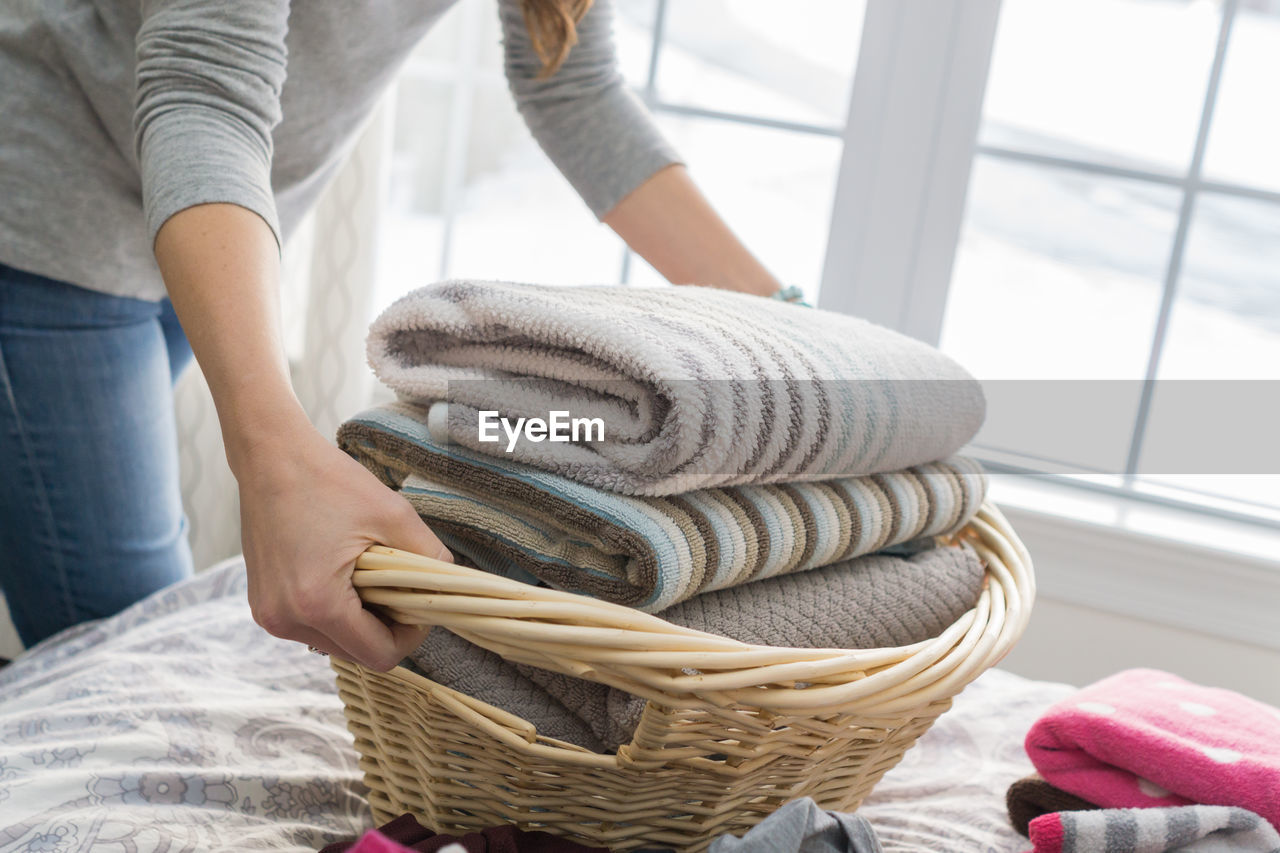 Midsection of woman holding laundry in wicker basket at home