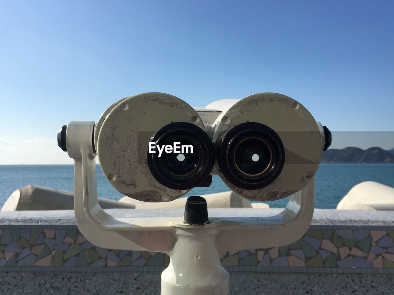 CLOSE-UP OF COIN-OPERATED BINOCULARS ON SEA AGAINST CLEAR SKY