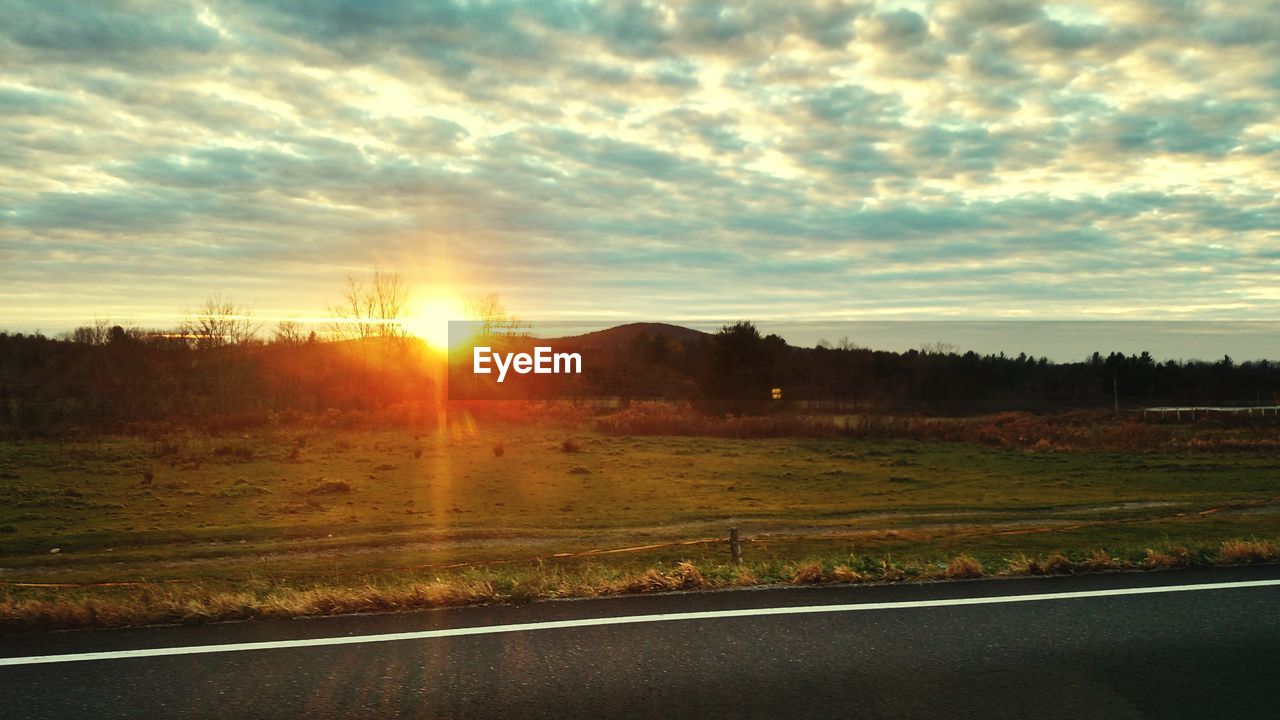 SUN SHINING THROUGH CLOUDS OVER FIELD