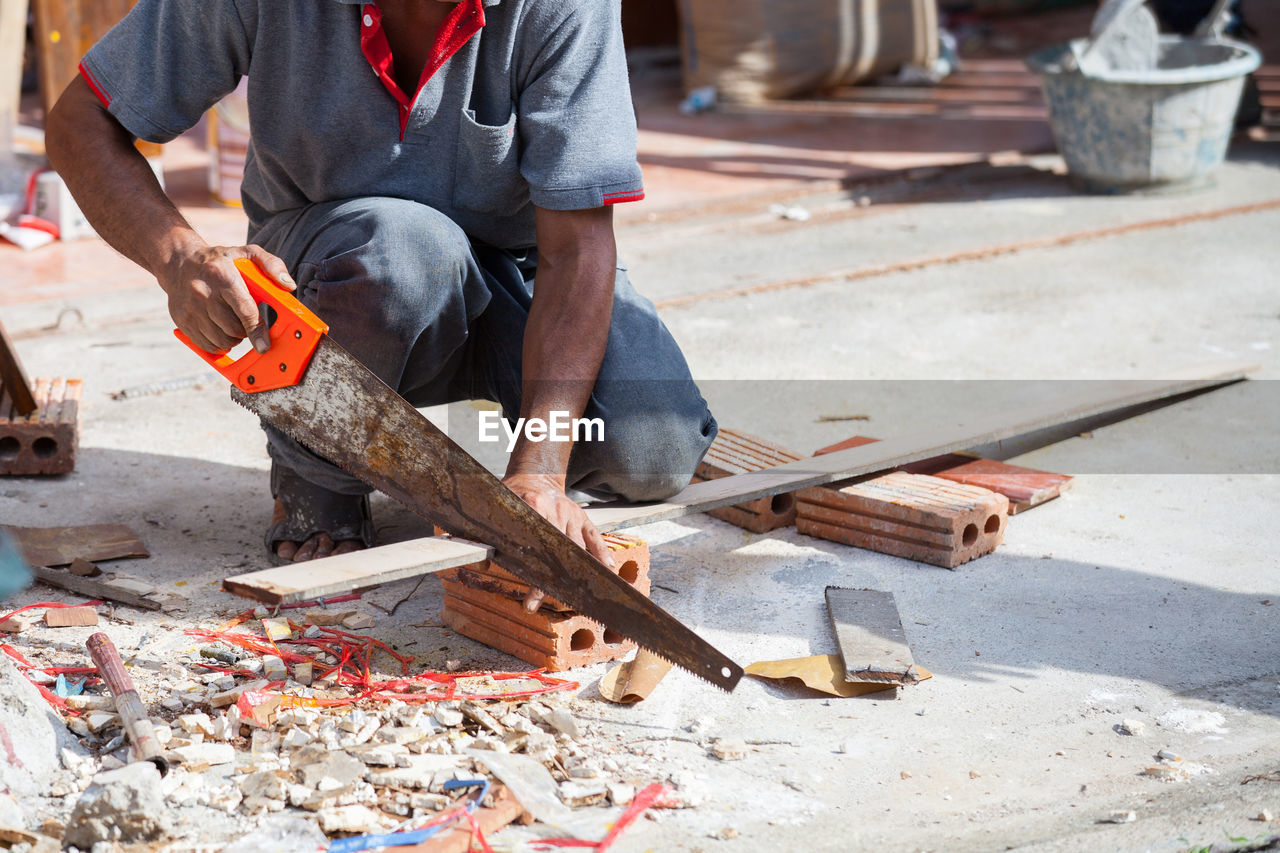 Low section of man cutting plank on floor