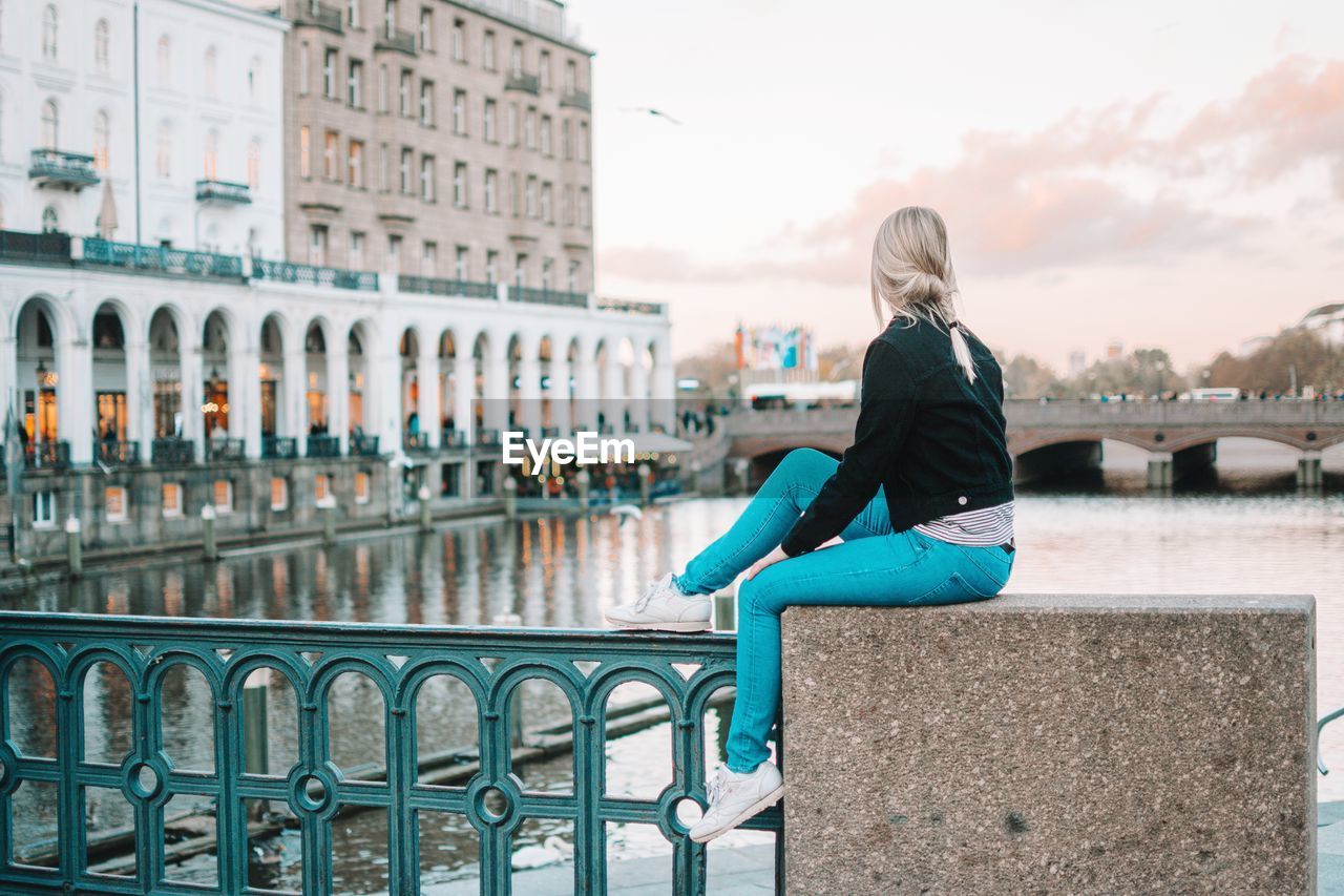 Young woman sitting on railing against sky