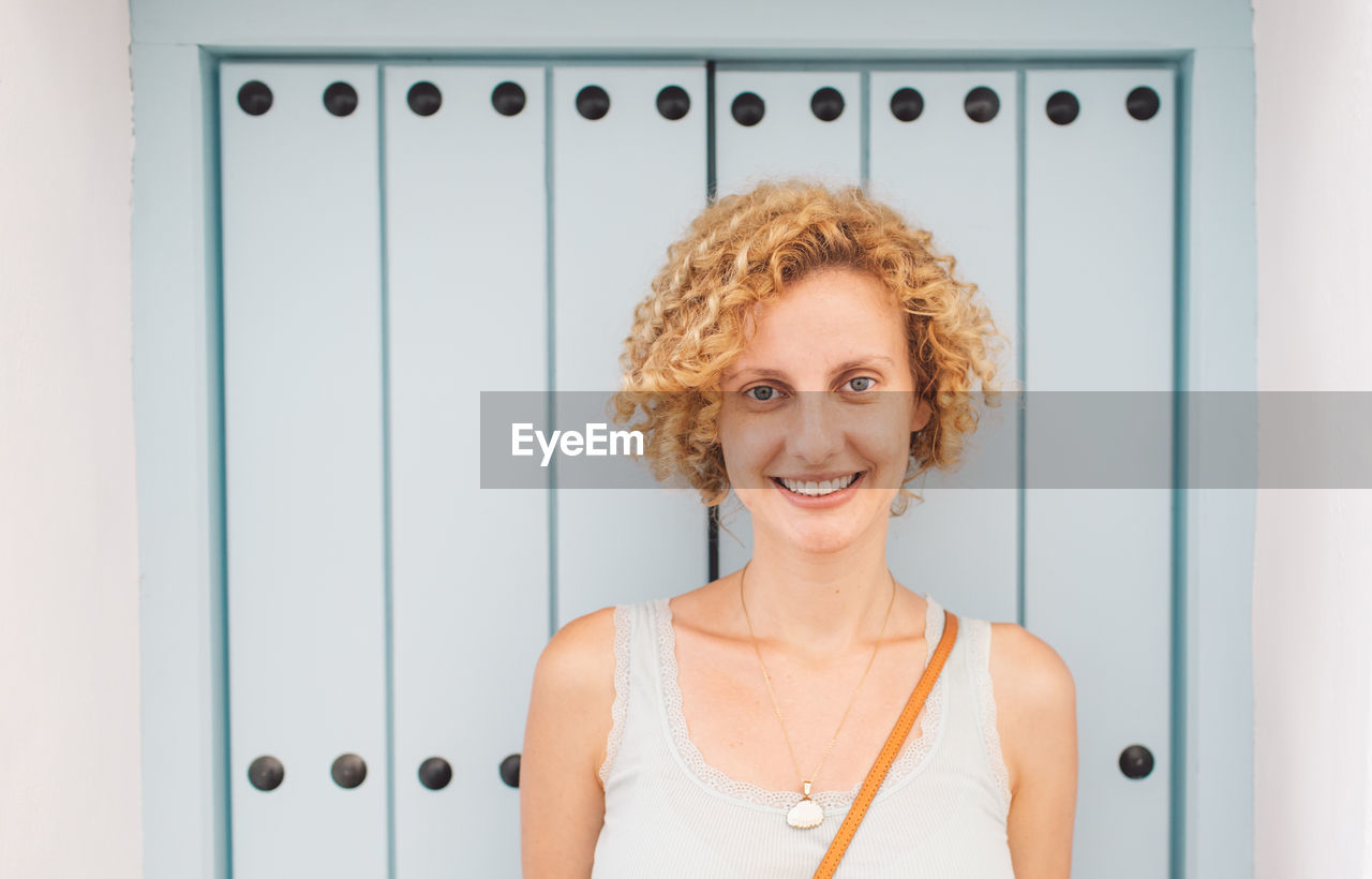 Portrait of smiling young woman standing by wall outdoors