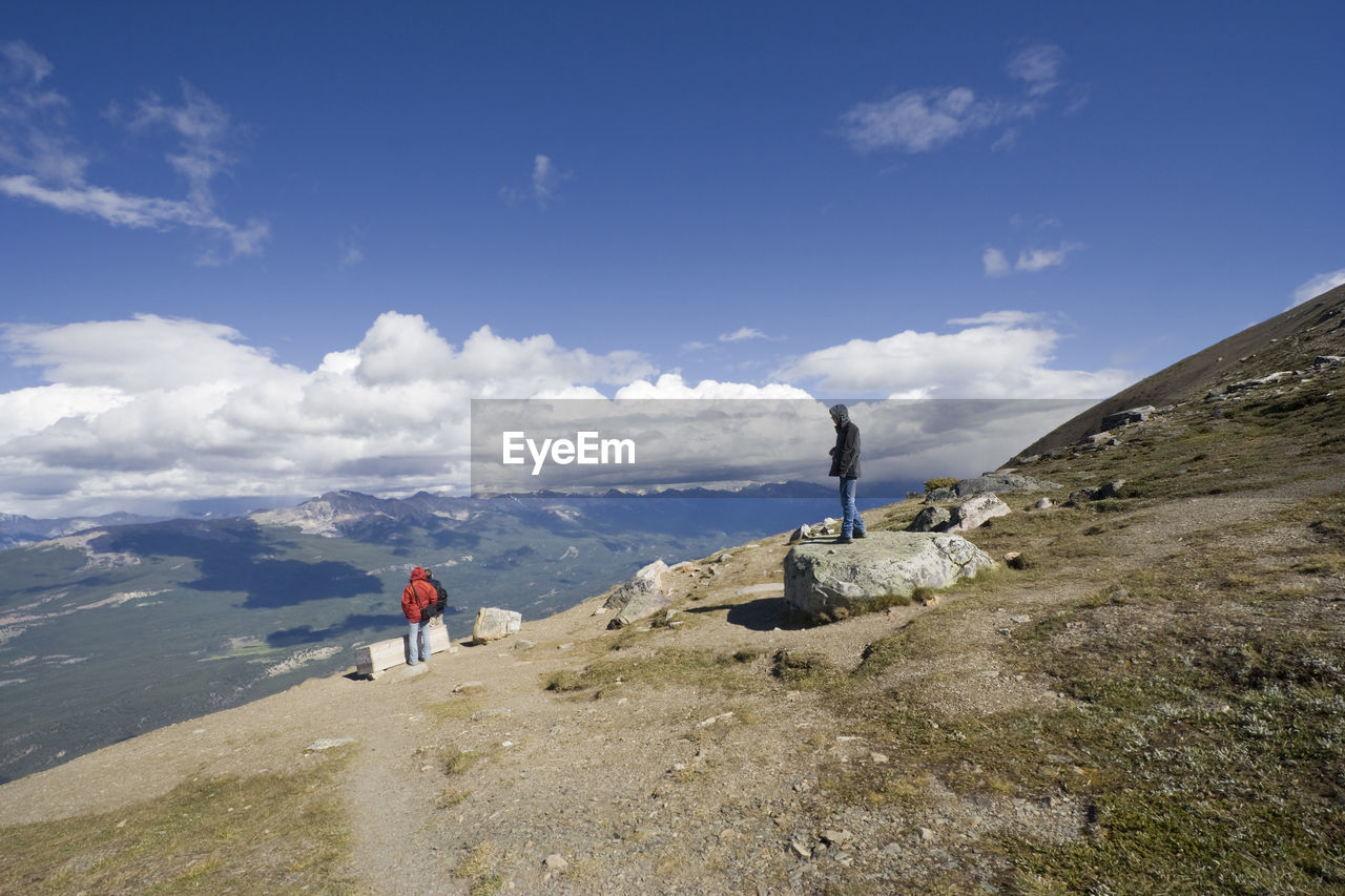 People standing on rocky mountain against cloudy sky at jasper national park