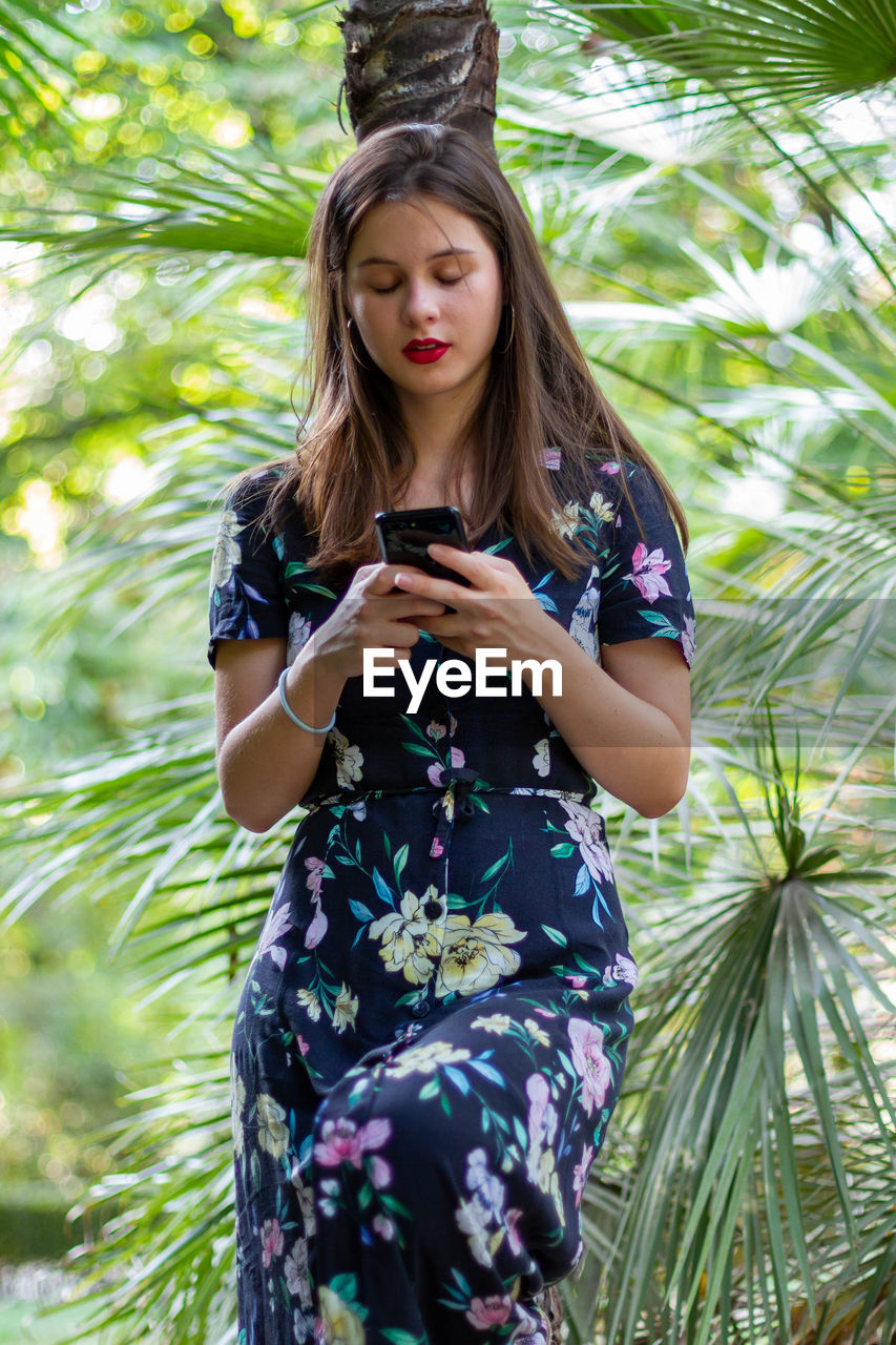 Young woman using mobile phone while standing against trees